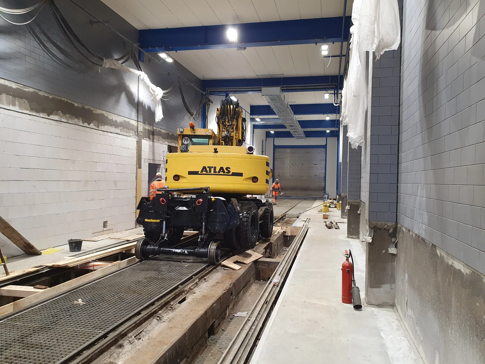 Zweiwegebagger bei Tiefbauarbeiten an Gleisen in einer Bahnhalle.