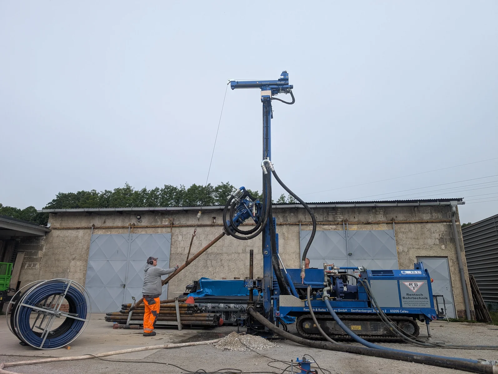 Blaue Erdwärme-Bohranlage mit senkrechtem Bohrmast auf einer Baustelle.